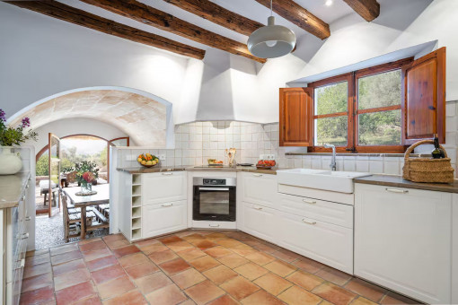 Cocina luminosa de estilo rústico con vigas de madera, suelo de terracota y acceso a la terraza