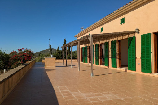 Terraza soleada de la finca con contraventanas verdes y pérgola, ideal para relajarse al aire libre